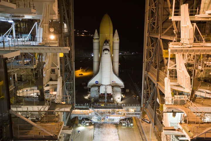 Image of a space shuttle stack in a vertical position leaving the large assembly building.