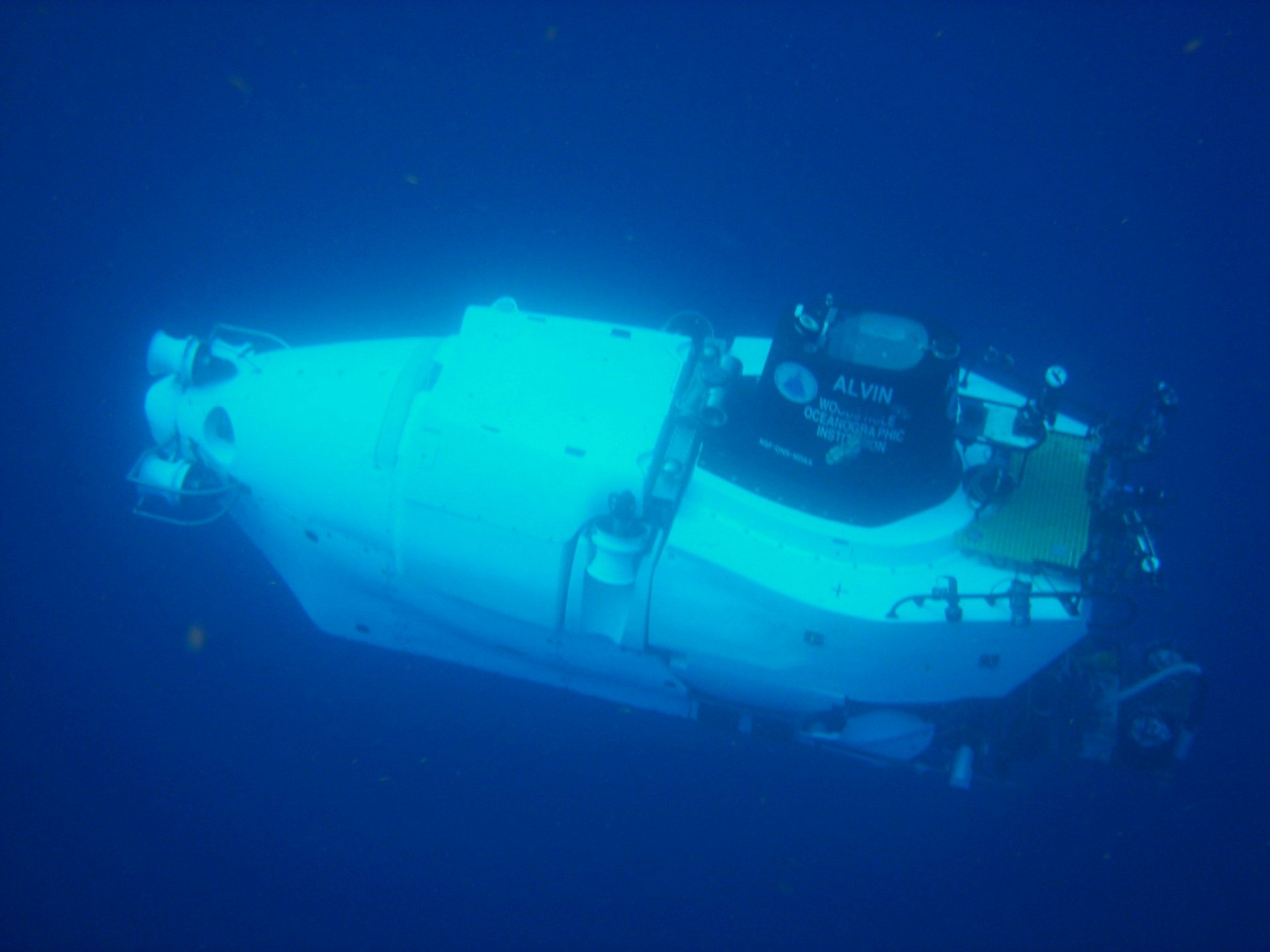 A small, cylindrical capsule with equipment attached to the top travels underwater.
